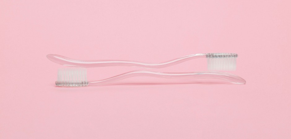 A photo of two toothbrushes on top of each other, in front of a light pink background.